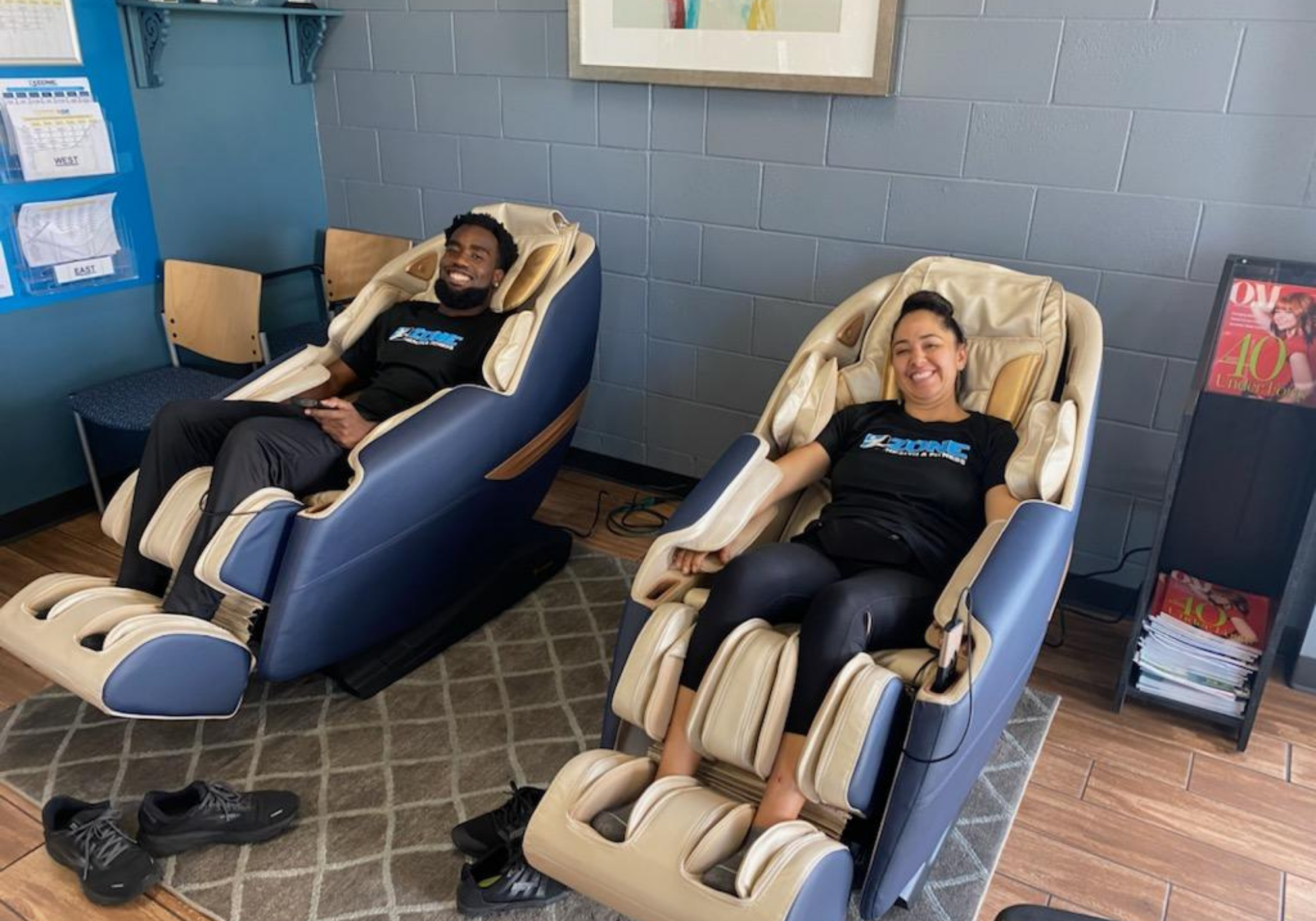 Two people relaxing in massage chairs in a room with blue walls and a tiled floor.