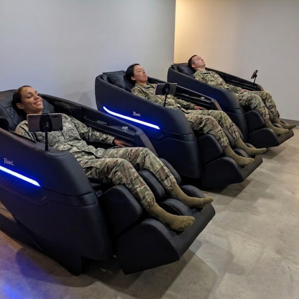 Three military service members in uniform utilizing Floridian Brand Rebel 4D massage chairs inside a dedicated base wellness center.