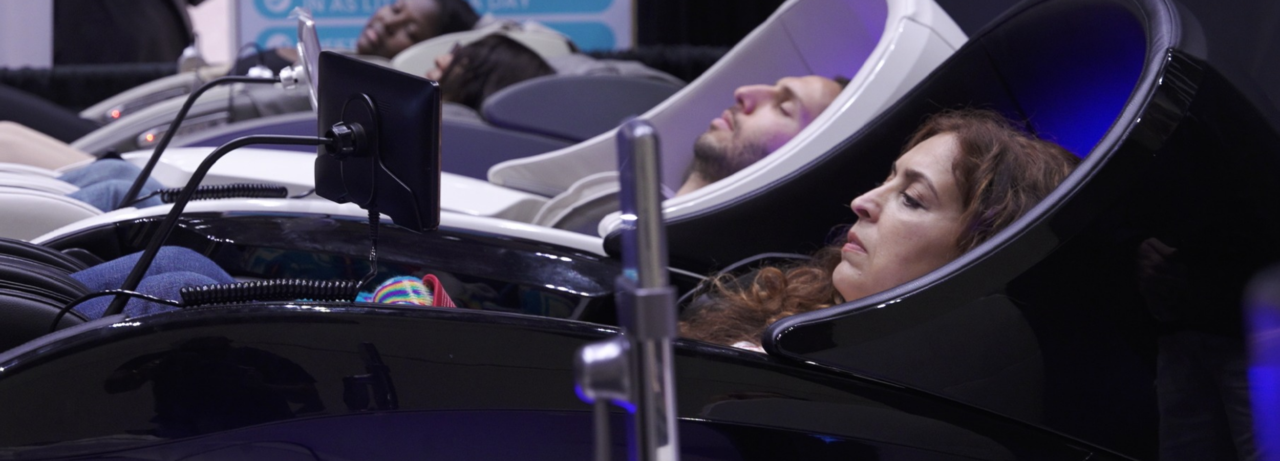 People lying down in futuristic pod chairs with screens, possibly in a sleep lab or technology demonstration setting.