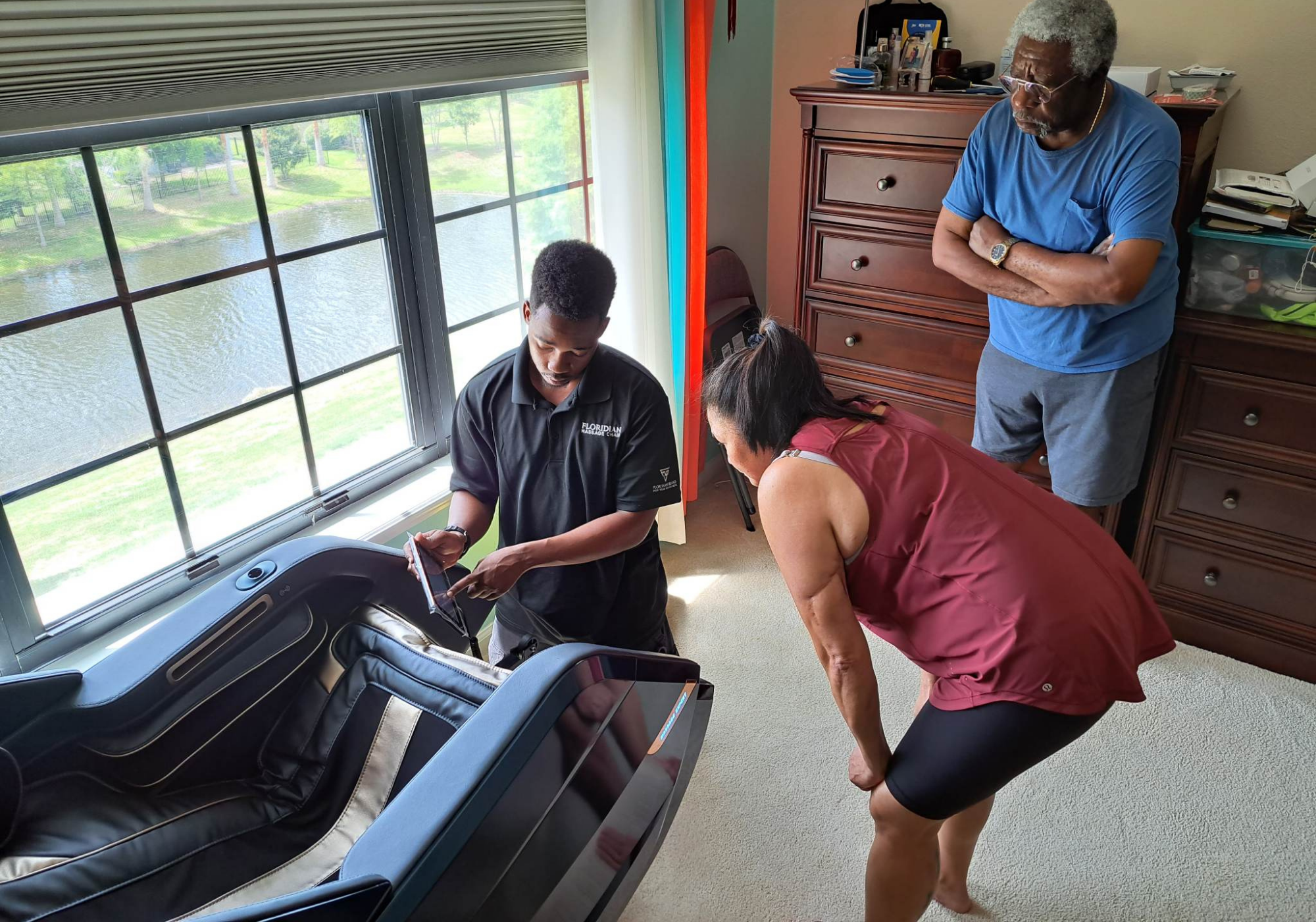 Two men and a woman working on a treadmill in a room with large windows and furniture.