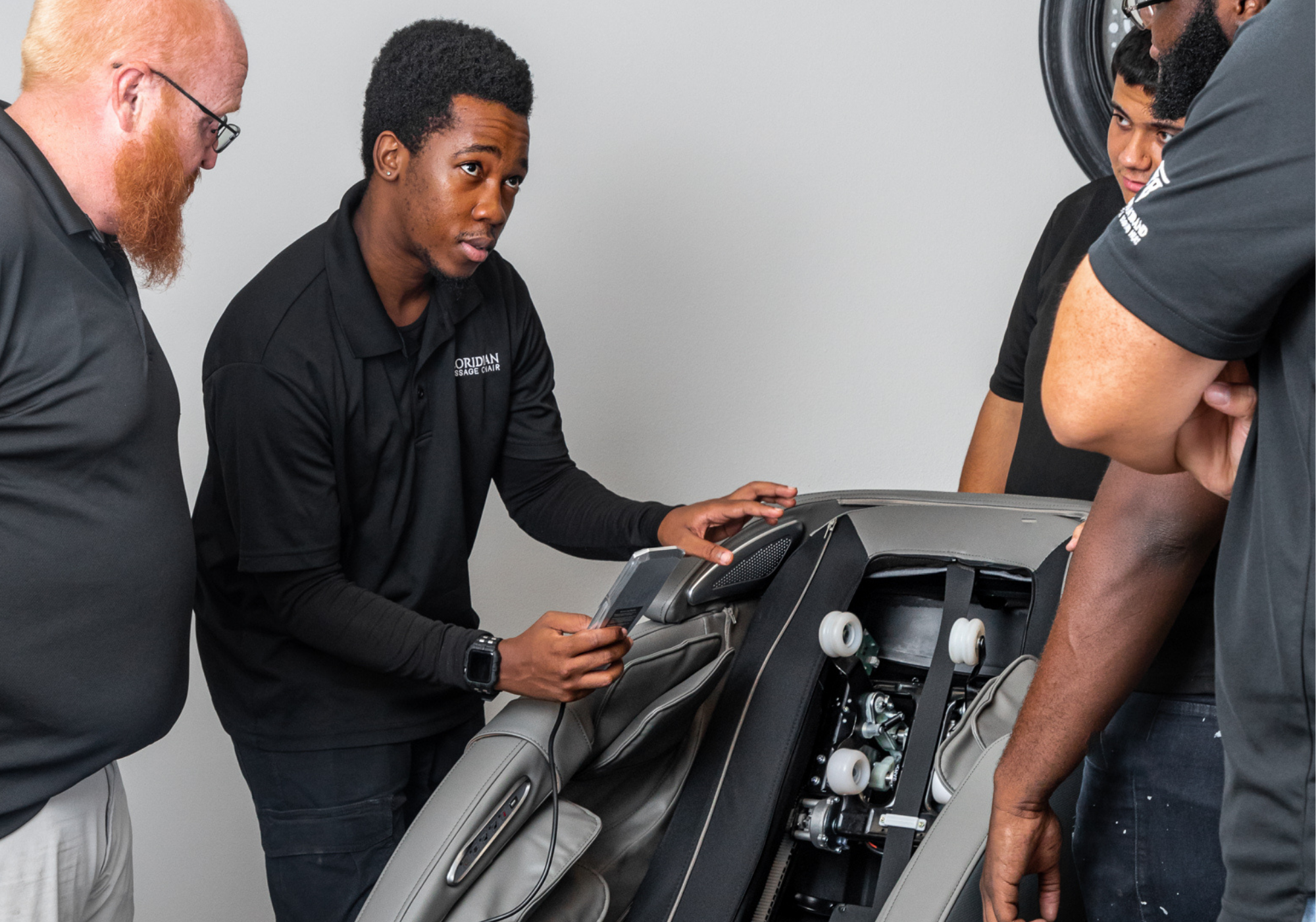Floridian Brand USA technician demonstrating massage chair repair and service training on an open chair with team members observing.