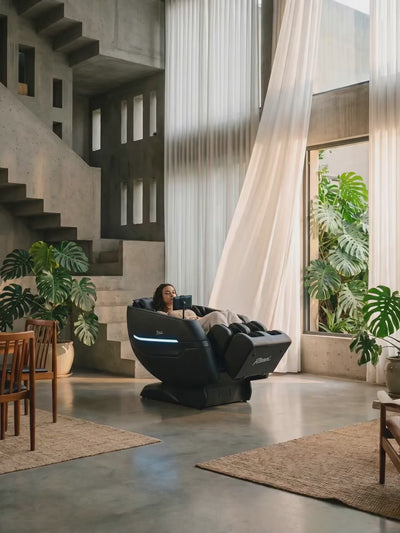 Rebel 4D massage chair in zero gravity recline with a woman relaxing in a premium dark studio